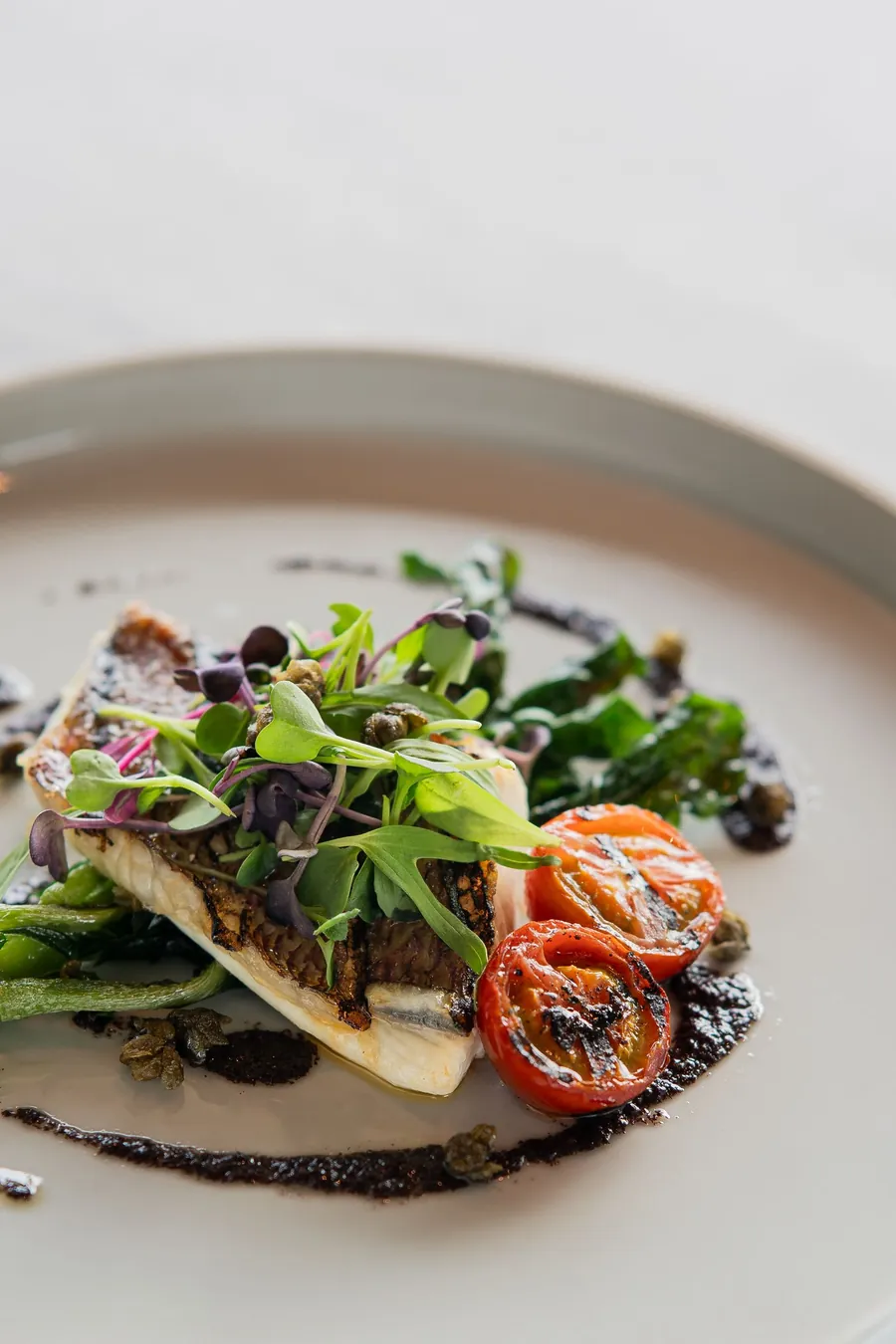 Filete de pescado sellado con hojas verdes y tomates asados